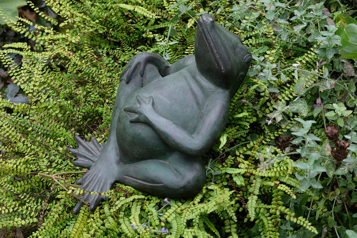 Bronze sculpture of a relaxing frog with green patina among ferns, perfect for indoor and outdoor decor.