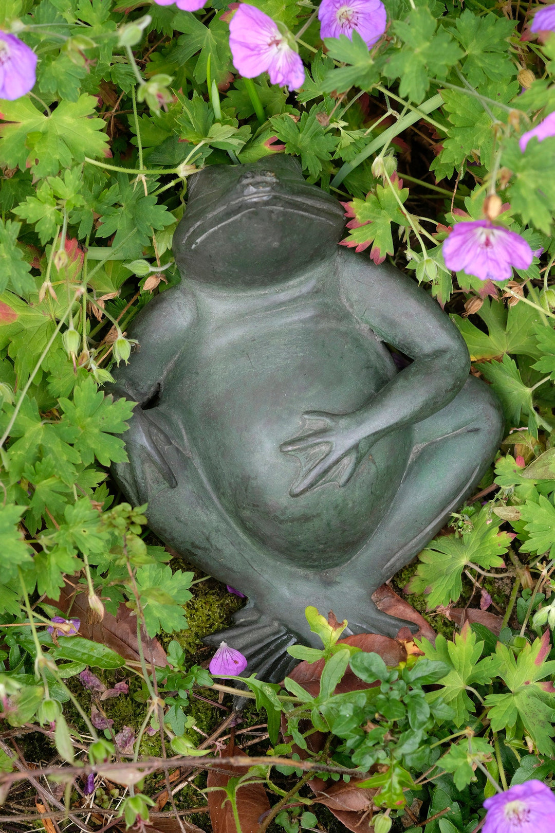 Bronze sculpture of a relaxing frog surrounded by vibrant flowers, showcasing a joyful art piece for indoor and outdoor decor.