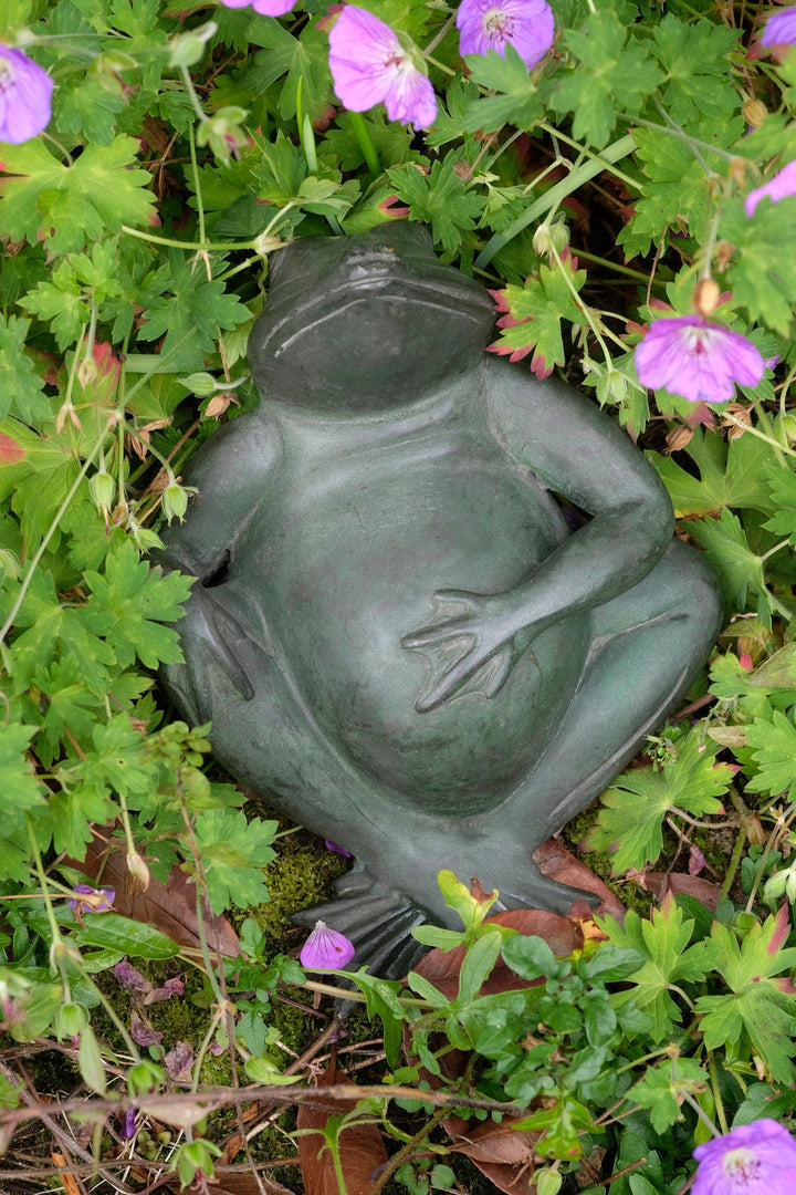 Bronze sculpture of a relaxing frog surrounded by vibrant flowers, showcasing a joyful art piece for indoor and outdoor decor.