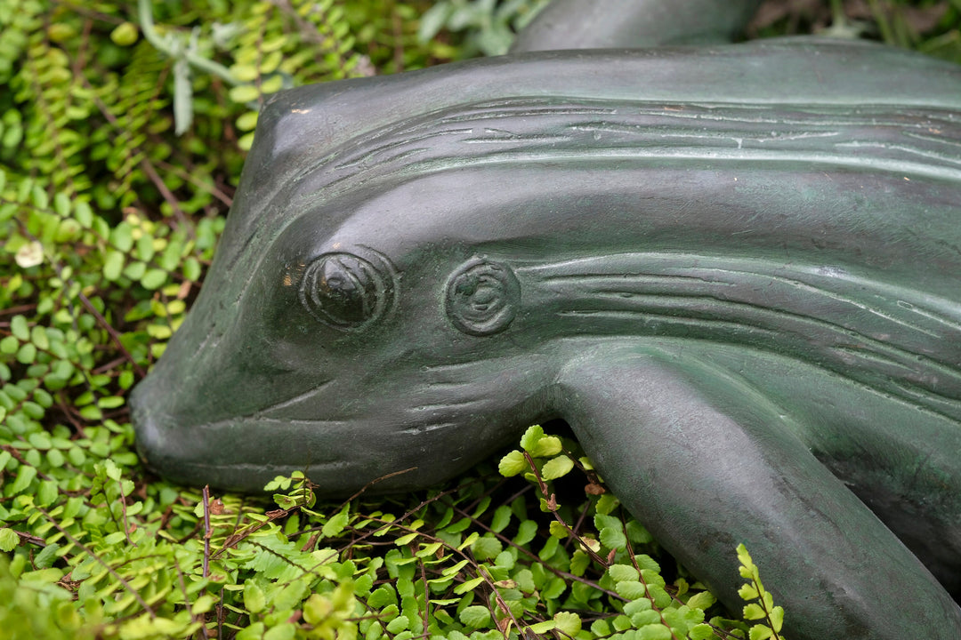 Bronze sculpture of a frog on green foliage, showcasing a relaxed pose with detailed craftsmanship.