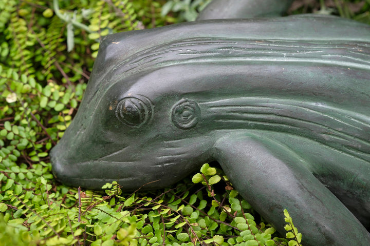 Bronze sculpture of a frog on green foliage, showcasing a relaxed pose with detailed craftsmanship.
