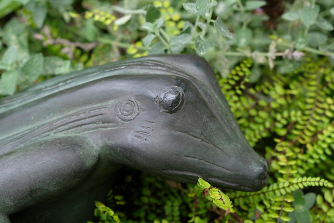 Close-up of a bronze frog sculpture nestled among greenery, showcasing intricate details and a serene expression.
