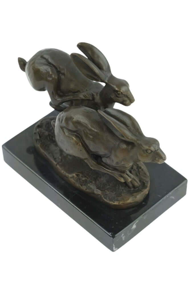Bronze sculpture of two running hares on a marble base, capturing a moment of action, signed by 'Nick'.