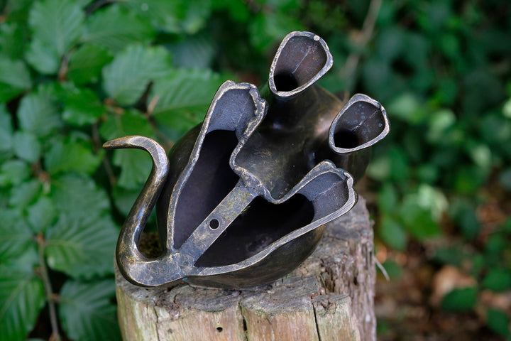 Bronze watering can sculpture with unique design, featuring spouts resembling floral shapes on a wooden stump.