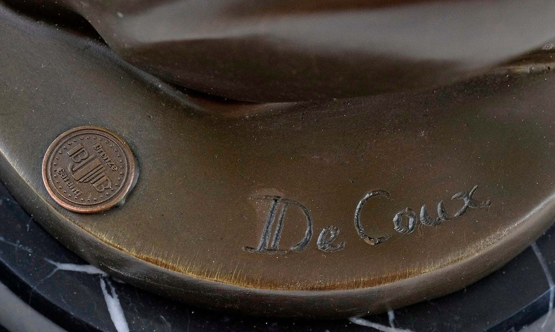 Close-up of the signature 'De Coux' and foundry stamp on a bronze sculpture base.