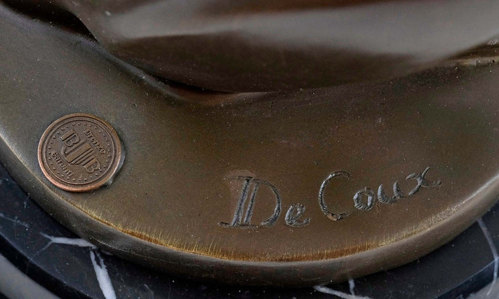 Close-up of the signature 'De Coux' and foundry stamp on a bronze sculpture base.