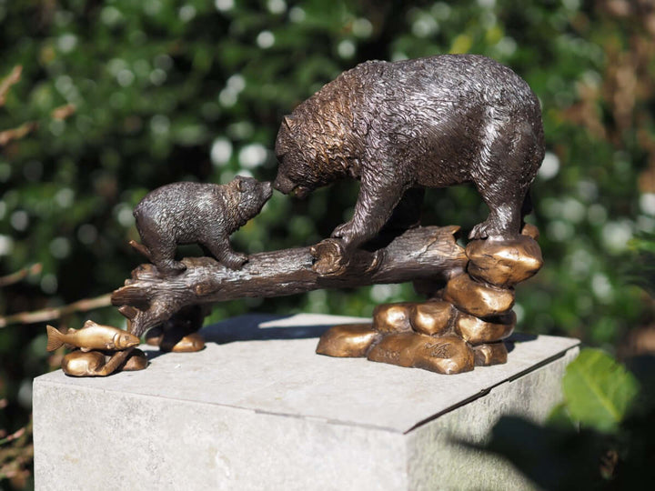 Bronze sculpture of a bear and cub on a tree trunk, capturing a tender moment in nature.