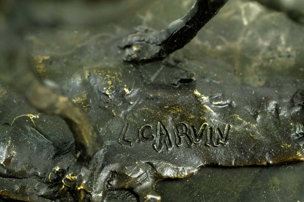 Close-up of the signature 'L. Carvin' on a bronze sculpture of a camel and rider, highlighting craftsmanship.
