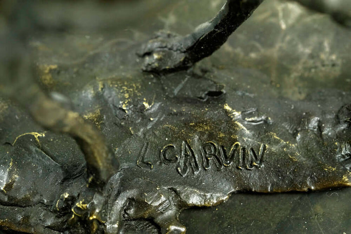 Close-up of the signature 'L. Carvin' on a bronze sculpture of a camel and rider, highlighting craftsmanship.