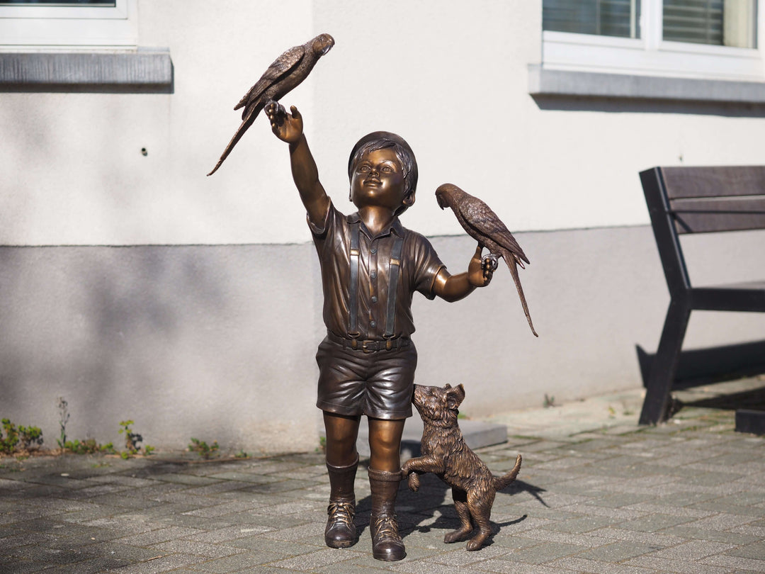 Bronze sculpture of a boy with parakeets and a playful dog, showcasing childhood innocence and joy.