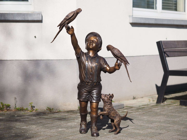 Bronze sculpture of a boy with parakeets and a playful dog, showcasing childhood innocence and joy.