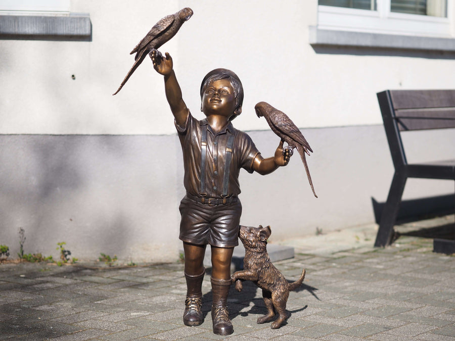 Bronze sculpture of a joyful boy holding parakeets with a playful dog at his feet, capturing childhood innocence.