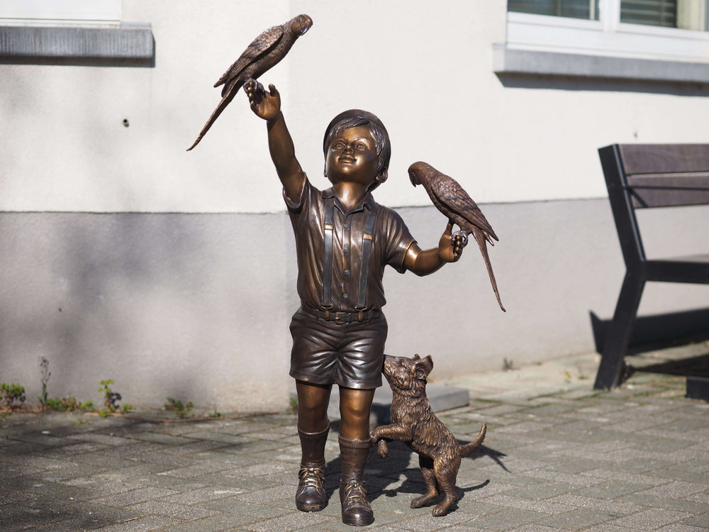 Bronze sculpture of a joyful boy with parakeets and a playful dog, highlighting childhood innocence and curiosity.