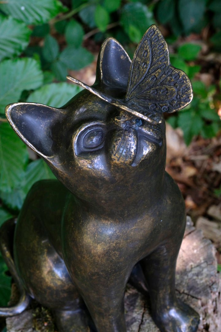 Bronze sculpture of a curious cat with a butterfly on its nose, showcasing playful elegance in home or garden decor.