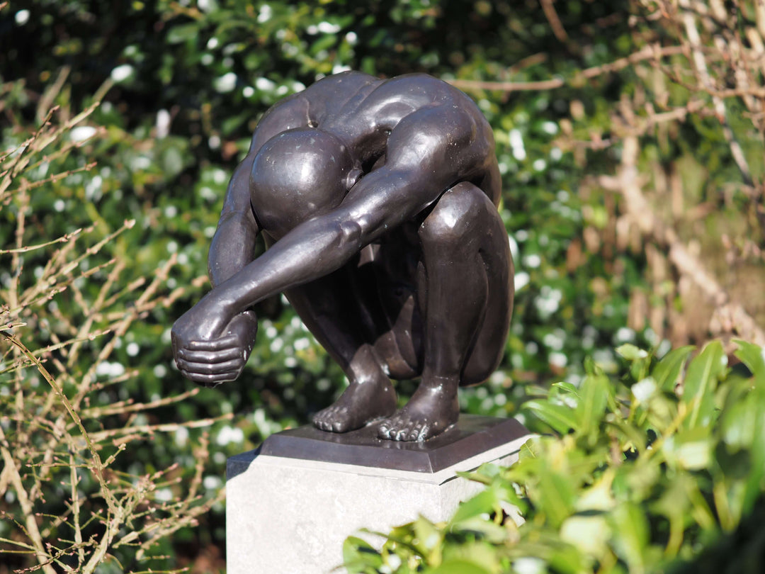 Bronze sculpture of a crouching man with outstretched arms, exuding balance and tranquility in a natural setting.