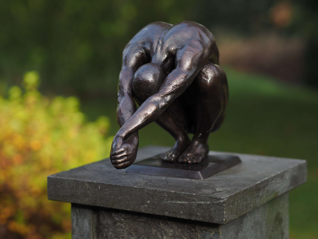 Bronze sculpture of a crouching man in balance, featuring dark patina, ideal for indoor and outdoor display.