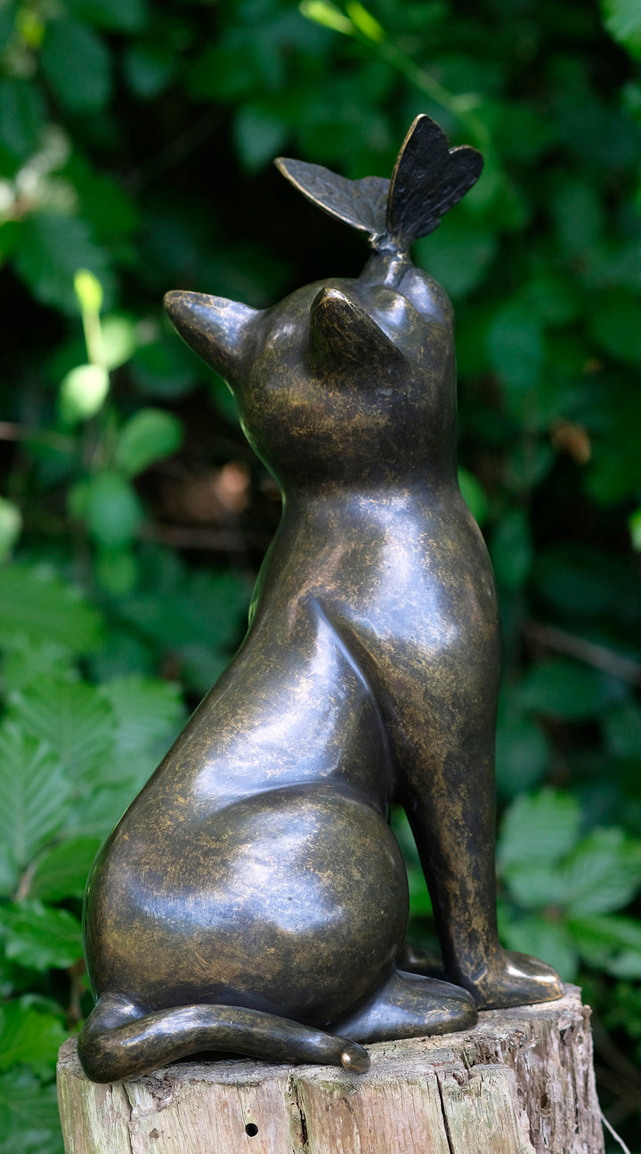 Bronze sculpture of a cat with a butterfly on its nose, showcasing playful elegance in nature.