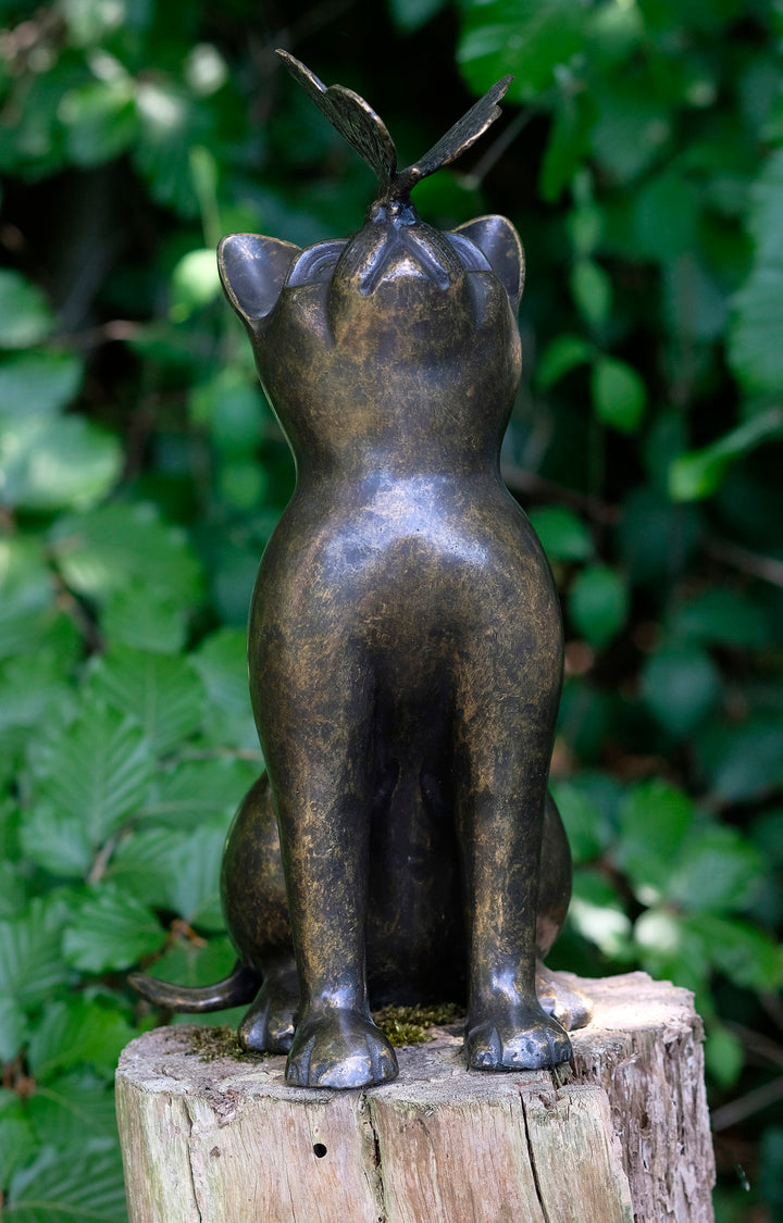 Bronze sculpture of a cat looking up at a butterfly, showcasing playful elegance in garden decor.