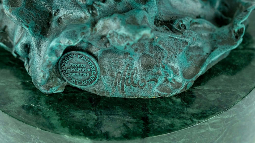 Close-up of bronze sculpture base showing artist's signature and foundry mark on textured surface.