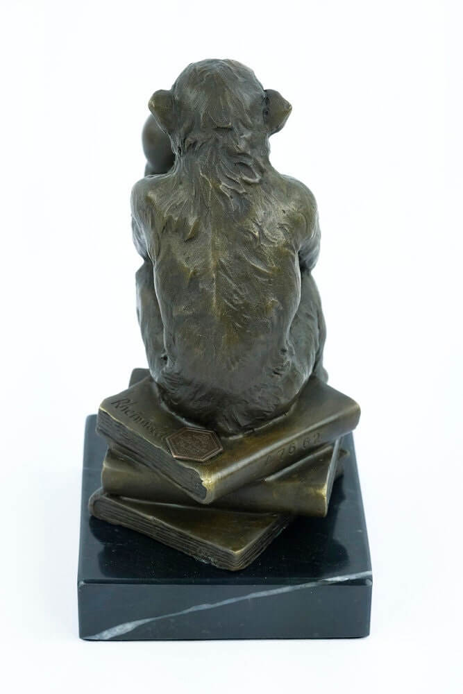 Bronze sculpture of a philosophizing monkey sitting on books, holding a skull, mounted on a black marble base.