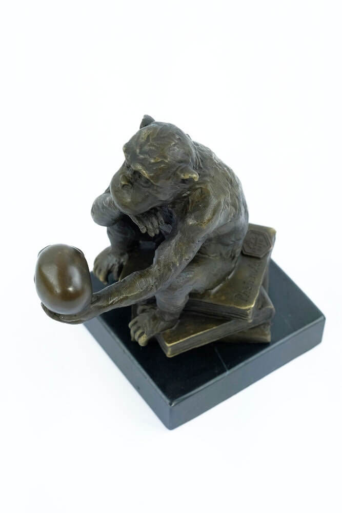 Bronze sculpture of a philosophizing monkey holding a skull, seated on books, mounted on a marble base.