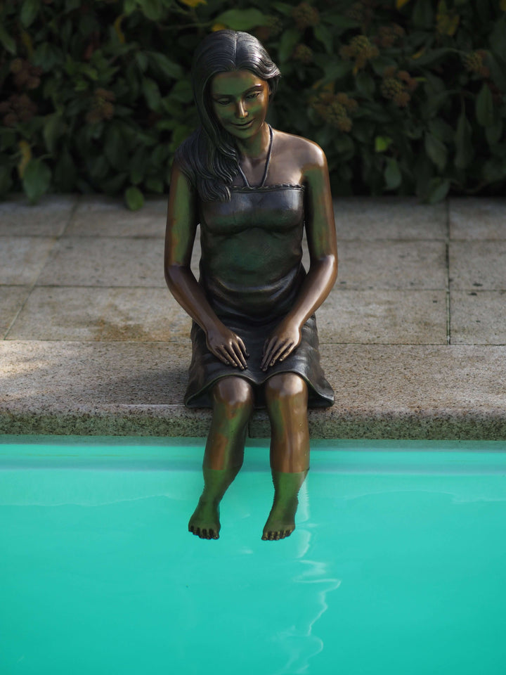 Bronze sculpture of a young woman sitting by a pool, elegantly posed with feet in water, showcasing fine craftsmanship.
