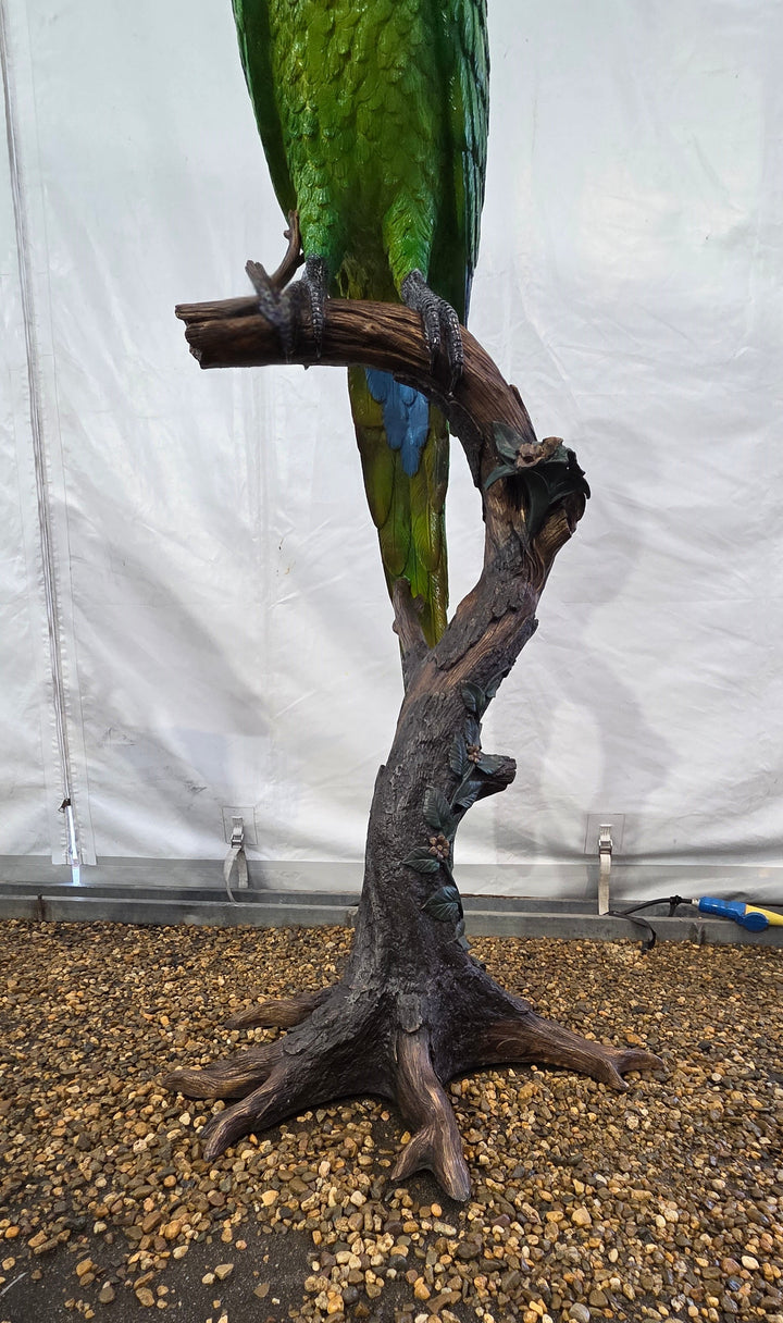 Large bronze sculpture of a green macaw on a tree trunk