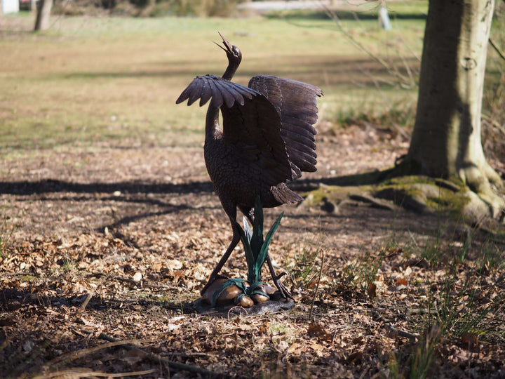 Elegant bronze stork sculpture with wings spread, serving as a fountain in a natural setting.