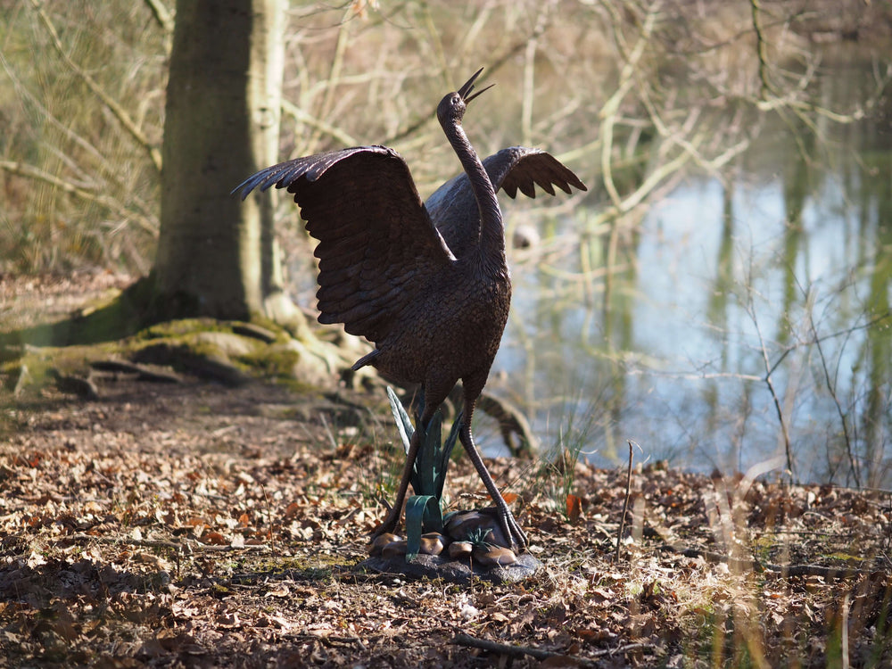 Graceful bronze stork fountain sculpture with wings spread near a tranquil water body, showcasing intricate details.