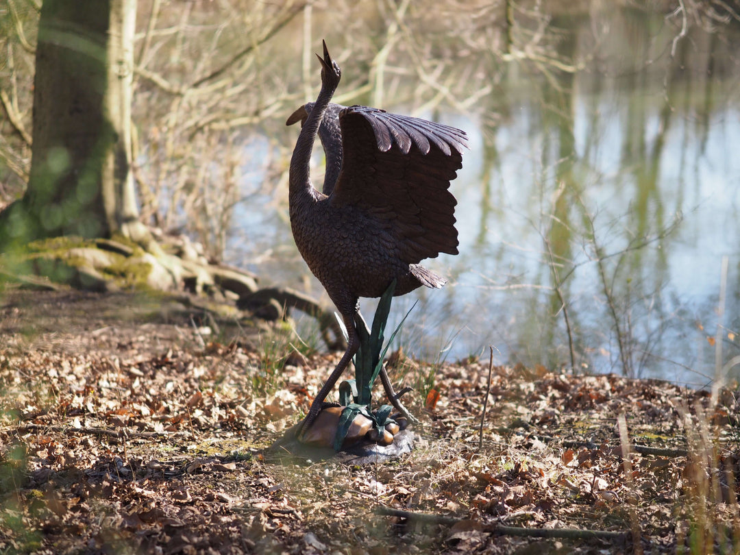 Elegant bronze stork fountain sculpture with spread wings near water, showcasing fine details in nature.
