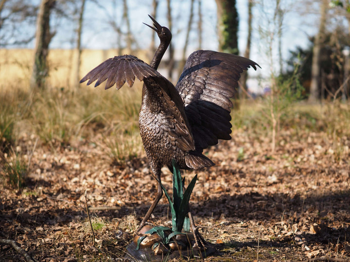 Elegant bronze stork fountain sculpture with wings spread, showcasing fine details in a natural setting.