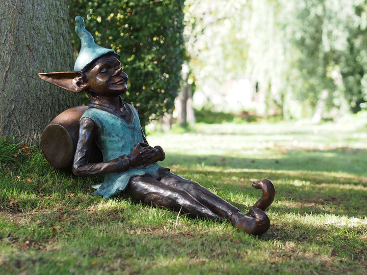 Bronze pixie sculpture lounging against a barrel, adding charm to any outdoor space. Dimensions: 100x40x57 cm.