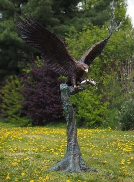 Large bronze sculpture of an eagle landing on a tree trunk, holding a fish, showcasing dynamic wings and fine detail.