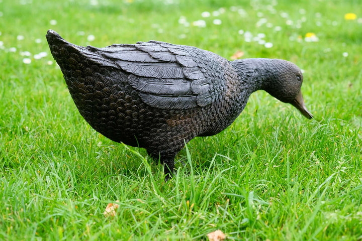 Lifesize bronze sculpture of a foraging duck in a grassy garden, showcasing detailed craftsmanship and quality.