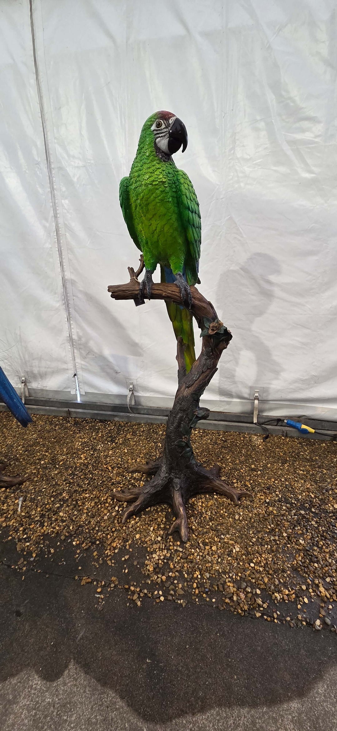 Lifesize bronze sculpture of a green macaw perched on a floral tree trunk, perfect for indoor or outdoor display.