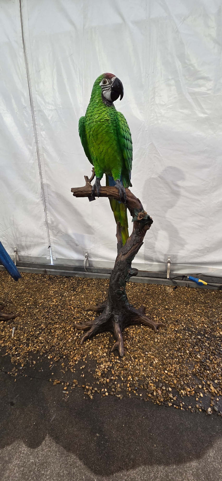 Lifesize bronze sculpture of a green macaw perched on a floral tree trunk, perfect for indoor or outdoor display.