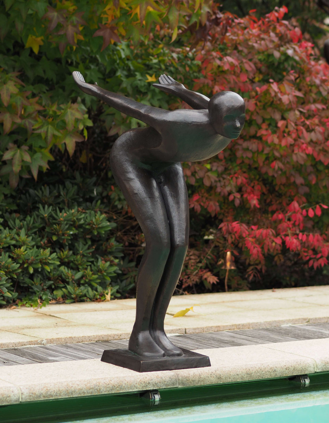 Large modern bronze sculpture of a poised swimmer beside a pool, showcasing elegance and artistry in outdoor decor.