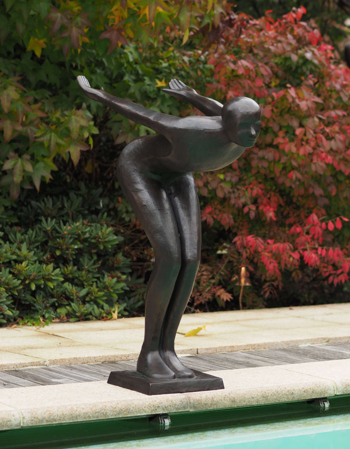 Large modern bronze sculpture of a poised swimmer beside a pool, showcasing elegance and artistry in outdoor decor.