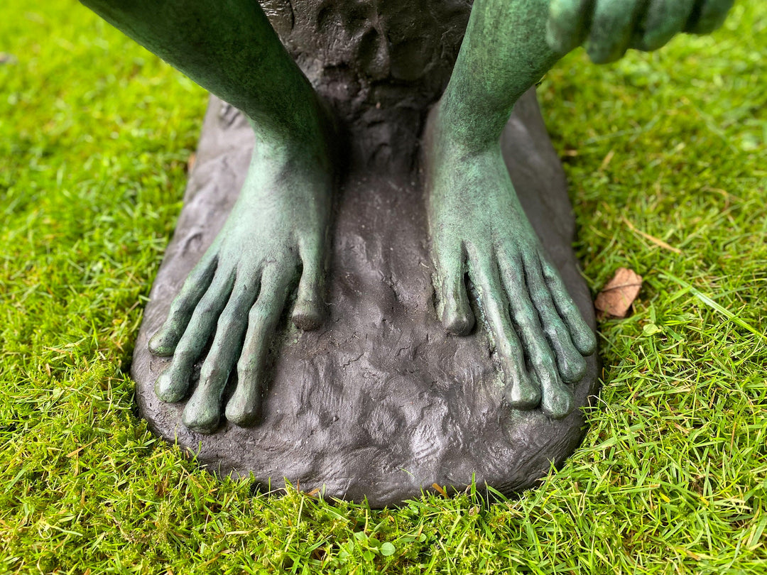 Close-up view of the feet of a large bronze frog sculpture on green grass, showcasing detailed craftsmanship.