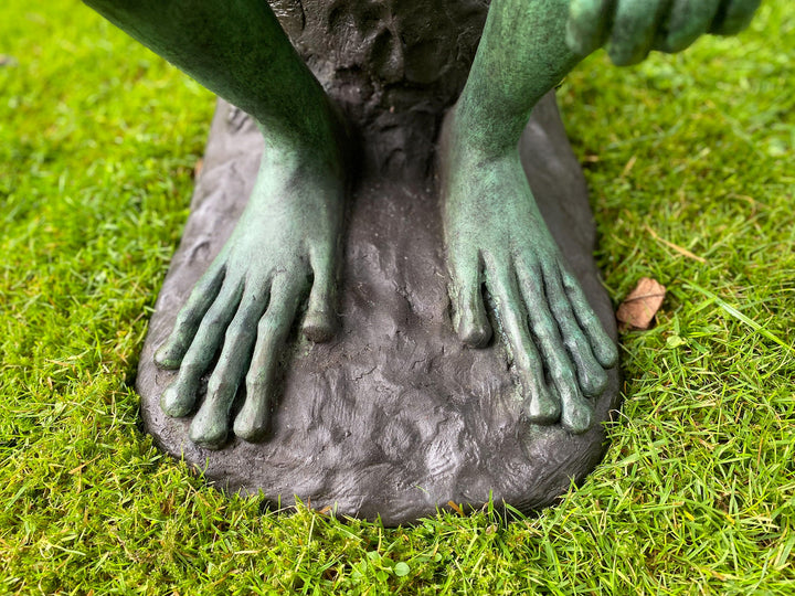 Close-up view of the feet of a large bronze frog sculpture on green grass, showcasing detailed craftsmanship.