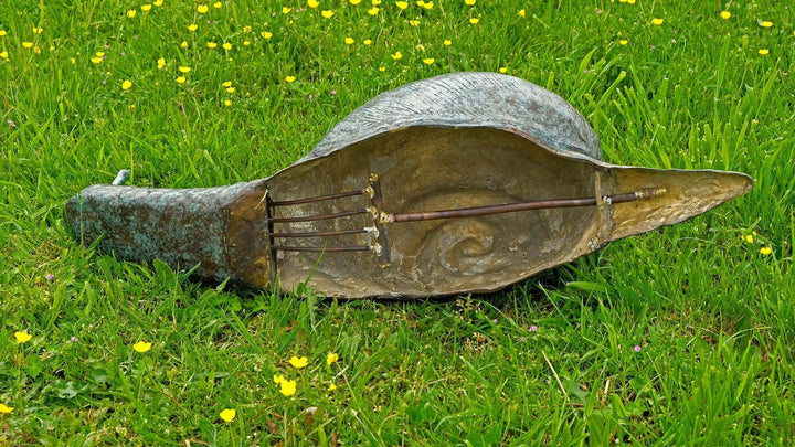 Large bronze snail sculpture interior view, showcasing water fountain features on grass with yellow flowers.