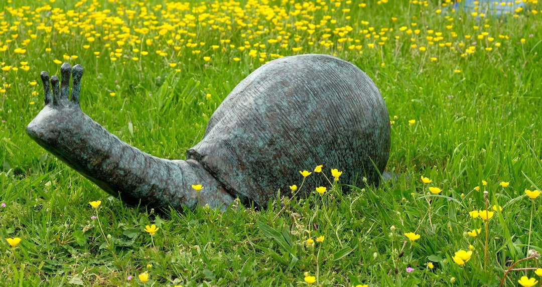 Large bronze snail sculpture in a garden with yellow wildflowers, perfect for outdoor decor and fountains.