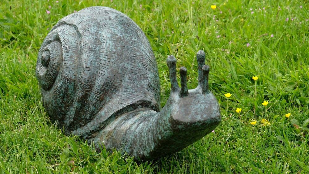 Large bronze snail sculpture in a garden, featuring mottled green patina and intricate detailing.