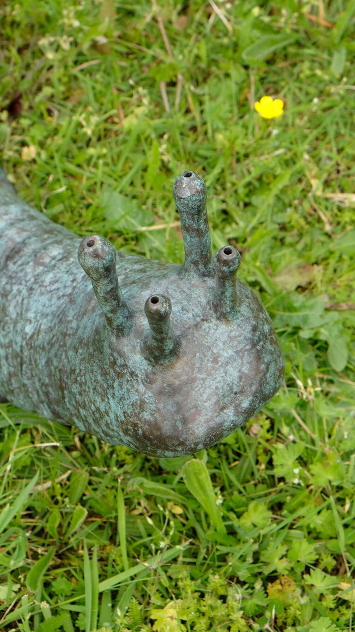 Large bronze snail sculpture fountain on grass, featuring a mottled green patina and intricate design.
