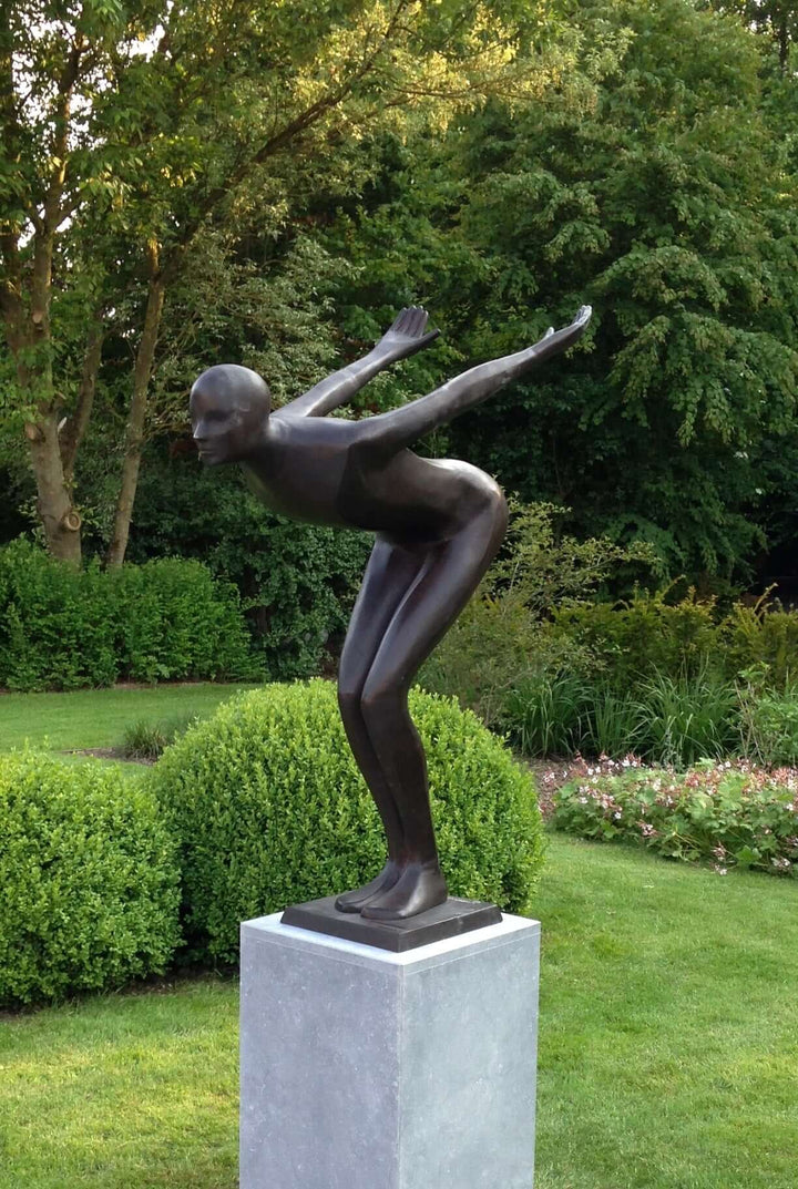 Large bronze sculpture of a poised swimmer in a garden, showcasing elegant form and sleek design.