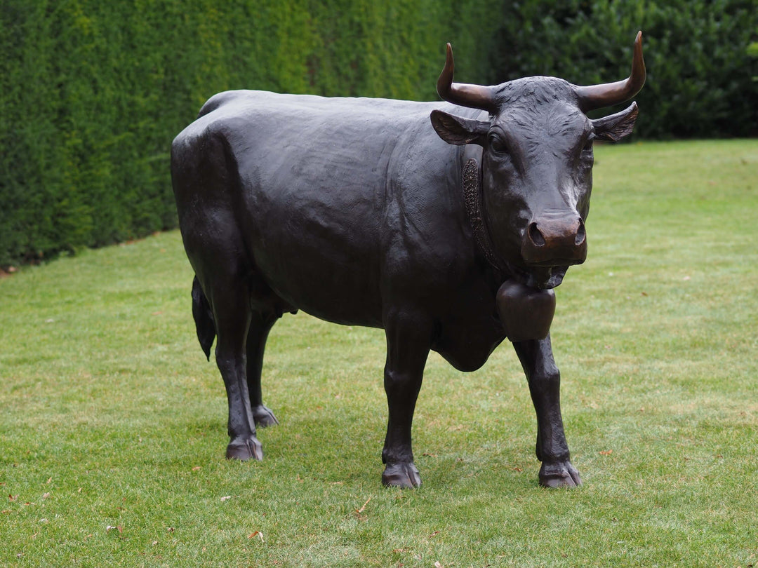 Lifesize bronze cow sculpture of Vache d’Hérens in garden, showcasing its muscular build and curved horns.