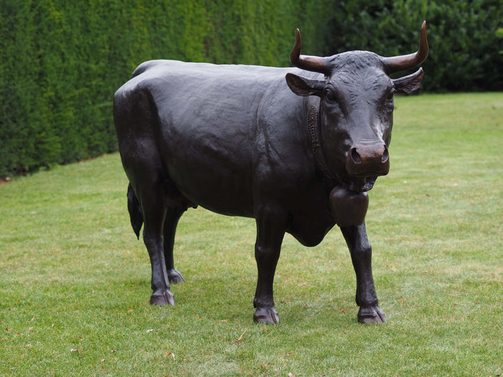 Lifesize bronze cow sculpture of Vache d’Hérens in garden, showcasing its muscular build and curved horns.