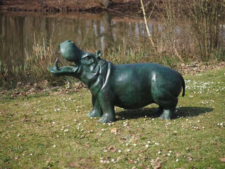 Lifesize bronze hippo sculpture fountain with rich green patina, situated on grass near a pond.