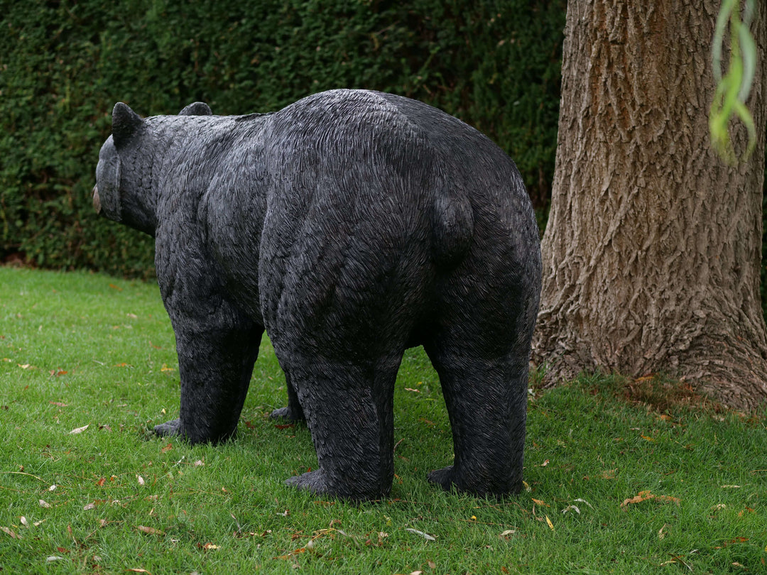 Lifelike bronze sculpture of a black bear outdoors, showcasing detailed features in a lush garden setting.