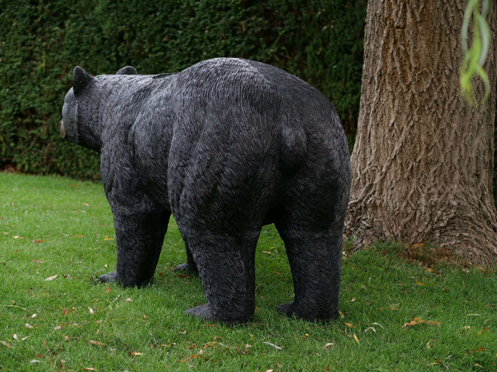 Lifelike bronze sculpture of a black bear outdoors, showcasing detailed features in a lush garden setting.